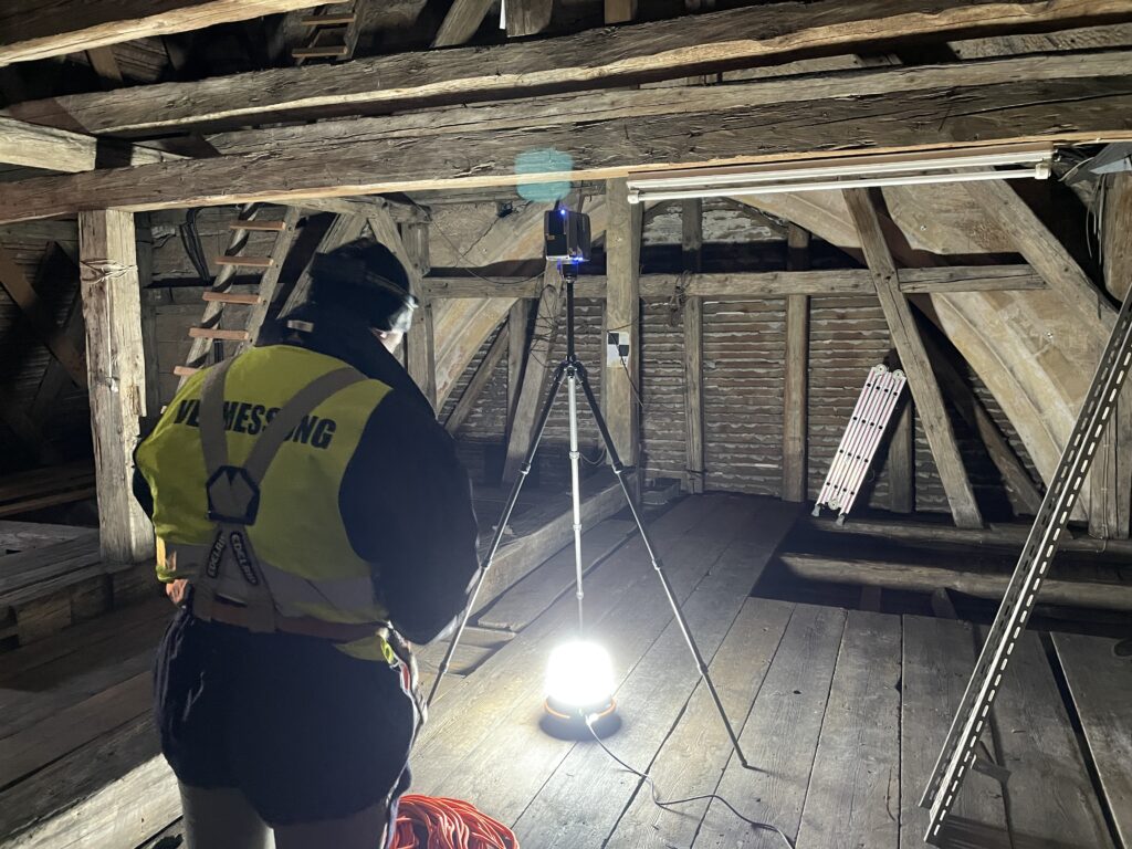 Surveyor in a high-visibility vest operating a scanner in a timber attic