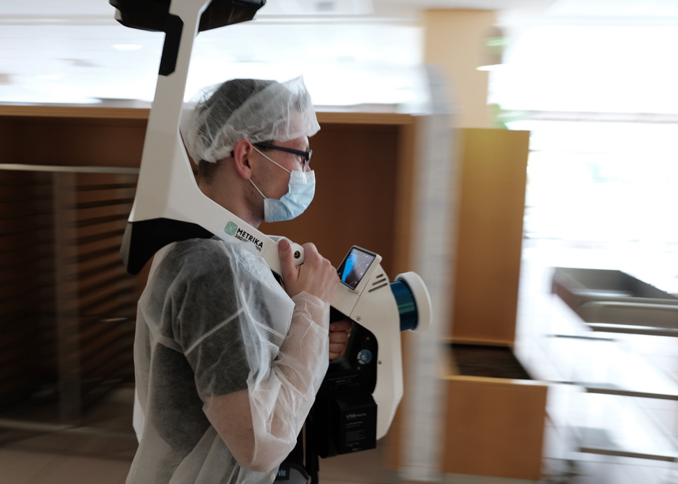 Operator in protective clothing carrying a mobile scanner through a clean room