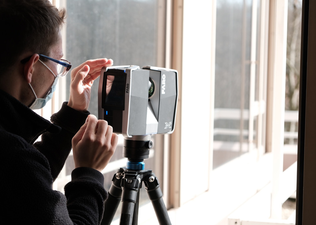 Surveyor operating a terrestrial laser scanner on a tripod beside a window